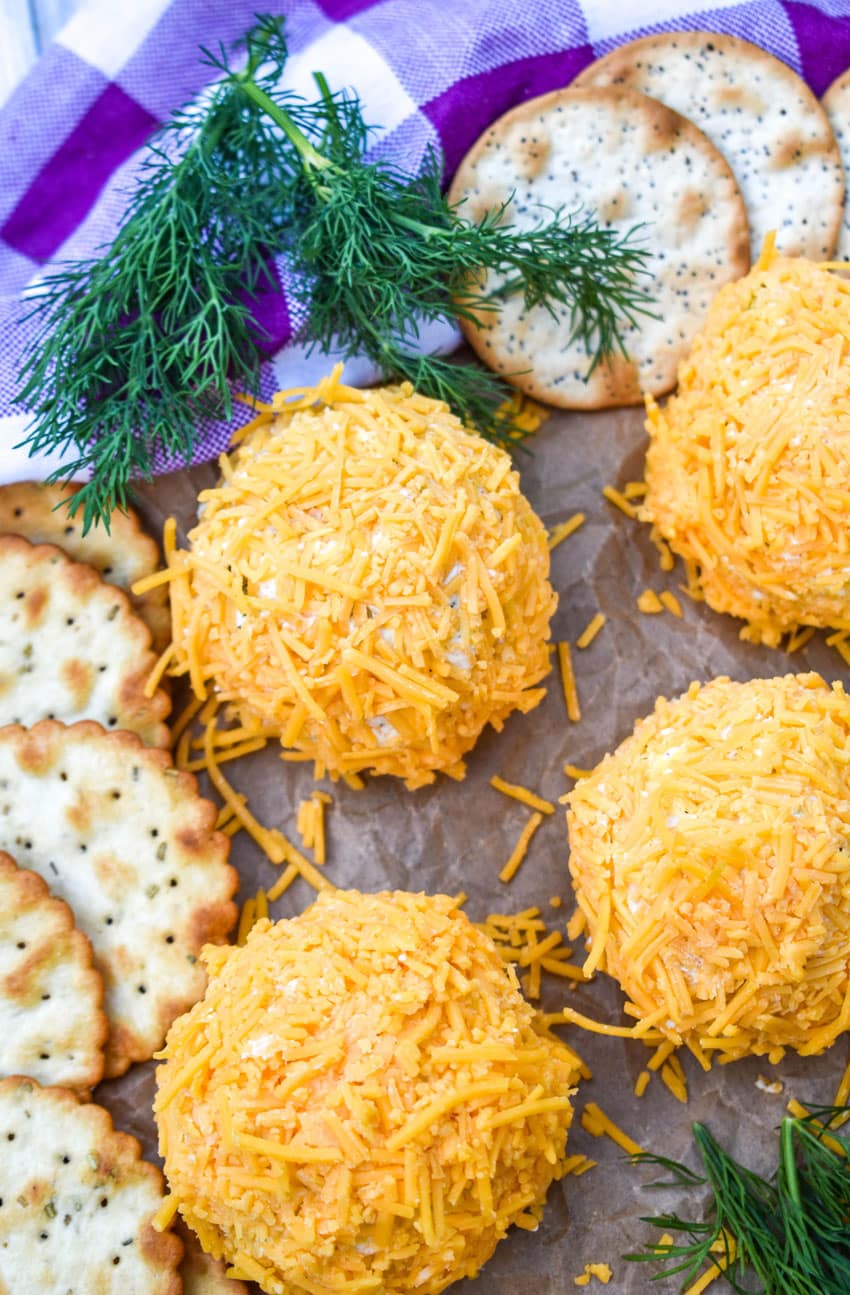 MINI DILL PICKLE CHEESE BALLS ON A WOODEN CUTTING BOARD WITH CRACKERS AND SPRIGS OF FRESH DILL ON THE SIDE
