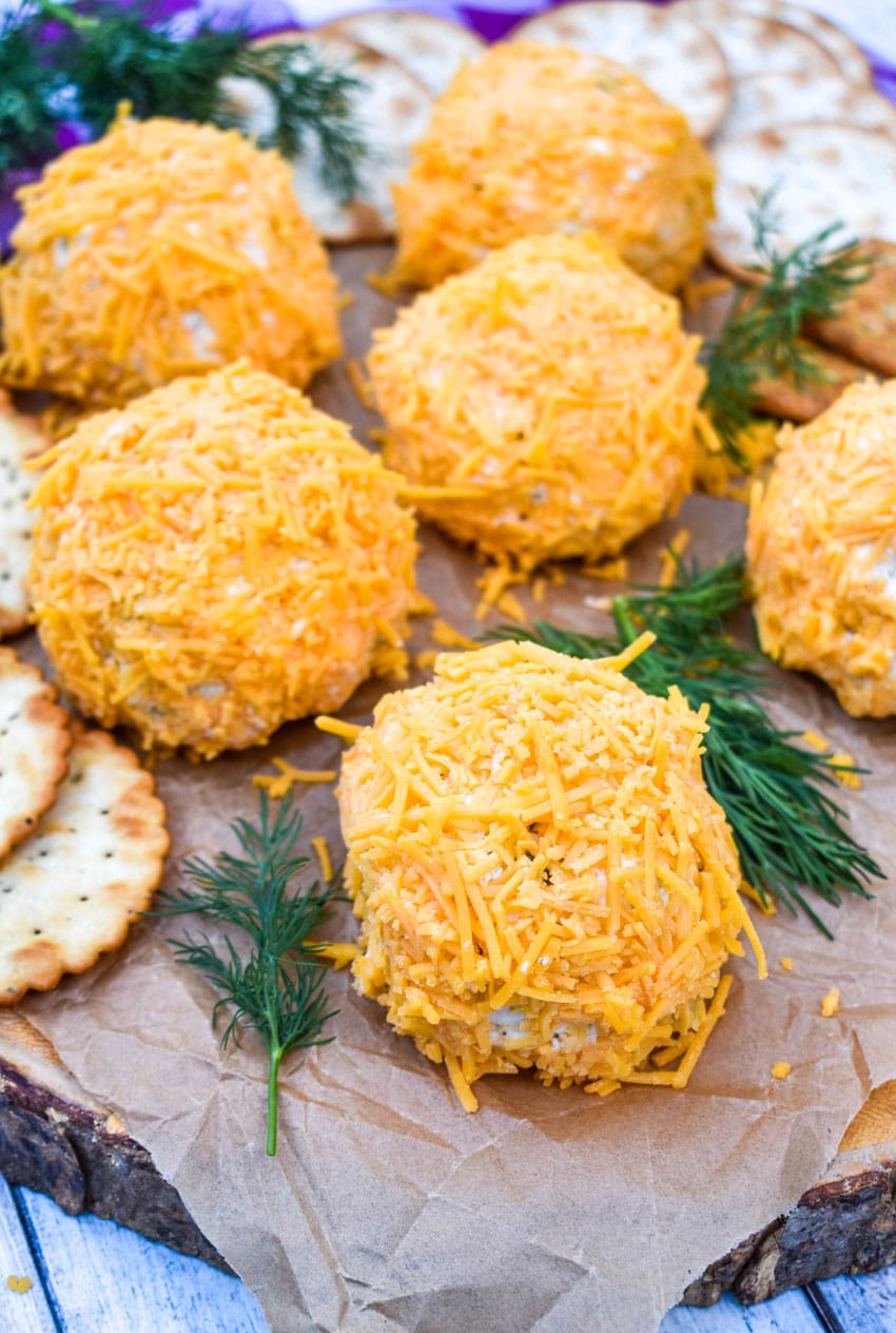 MINI DILL PICKLE CHEESE BALLS ON A WOODEN CUTTING BOARD WITH CRACKERS AND SPRIGS OF FRESH DILL ON THE SIDE