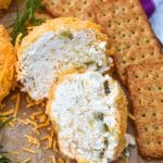 TWO HALVES OF A MINI DILL PICKLE CHEESE BALL ON A WOODEN CUTTING BOARD SURROUNDED BY ASSORTED CRACKERS