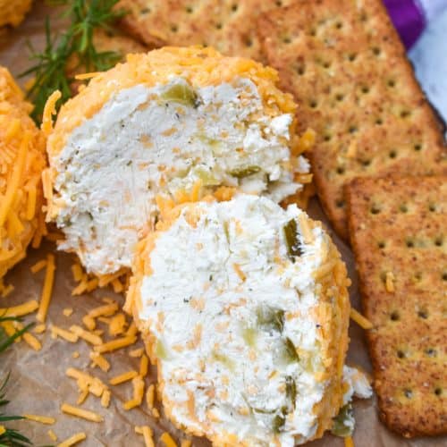 TWO HALVES OF A MINI DILL PICKLE CHEESE BALL ON A WOODEN CUTTING BOARD SURROUNDED BY ASSORTED CRACKERS