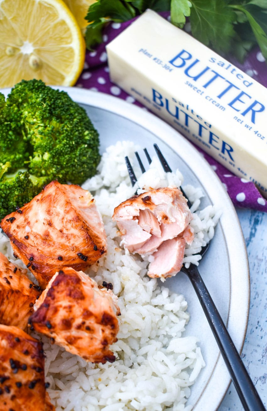 a black fork holding an piece of air fried salmon resting on the edge of a white plate