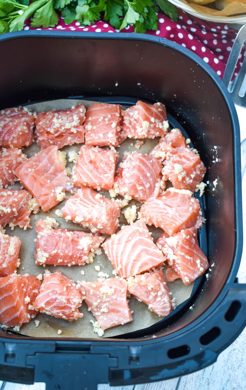 chunks of raw salmon coated with butter and minced garlic in the basket of an air fryer