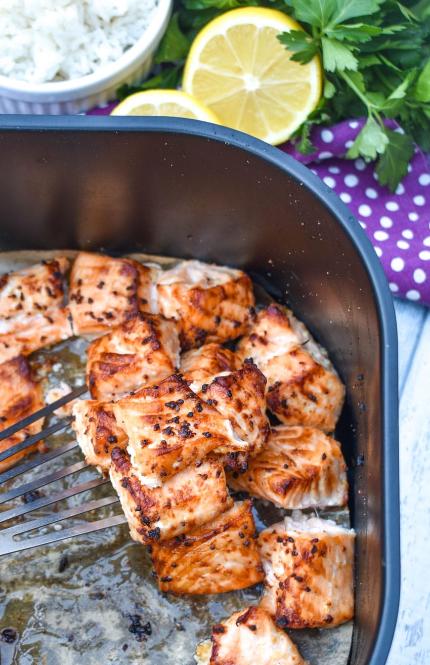 a fish spatula scooping lemon garlic air fryer salmon bites out of the basket of an air fryer