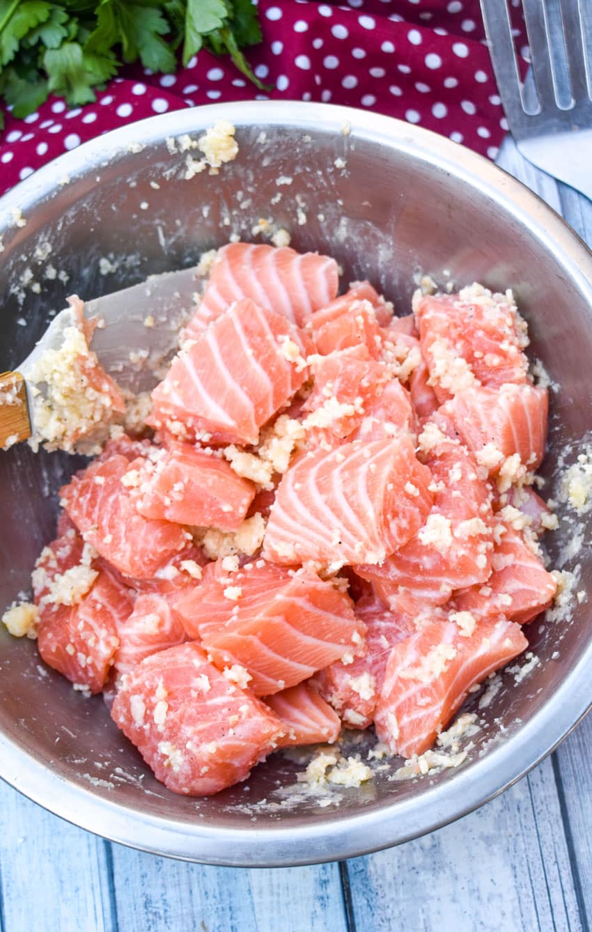 pieces of raw salmon coated with butter and minced garlic in a small metal bowl