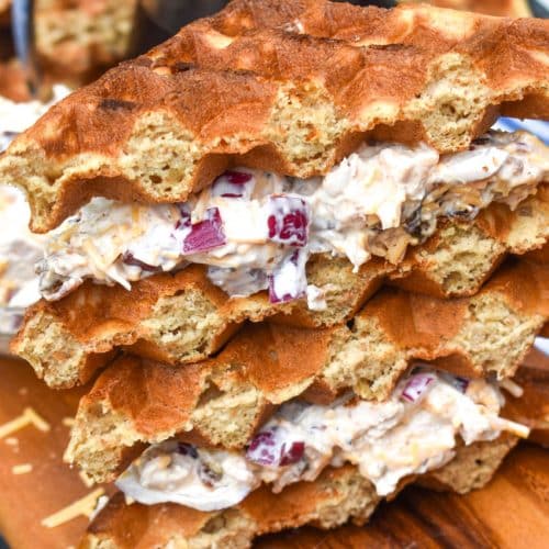 two maple bacon chicken salad waffle sandwiches stacked together on a wooden cutting board