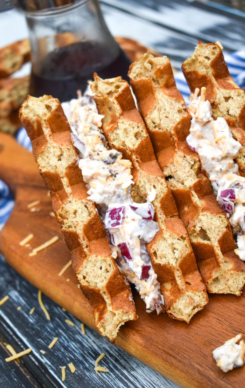 two maple bacon chicken salad waffle sandwiches stacked together on a wooden cutting board