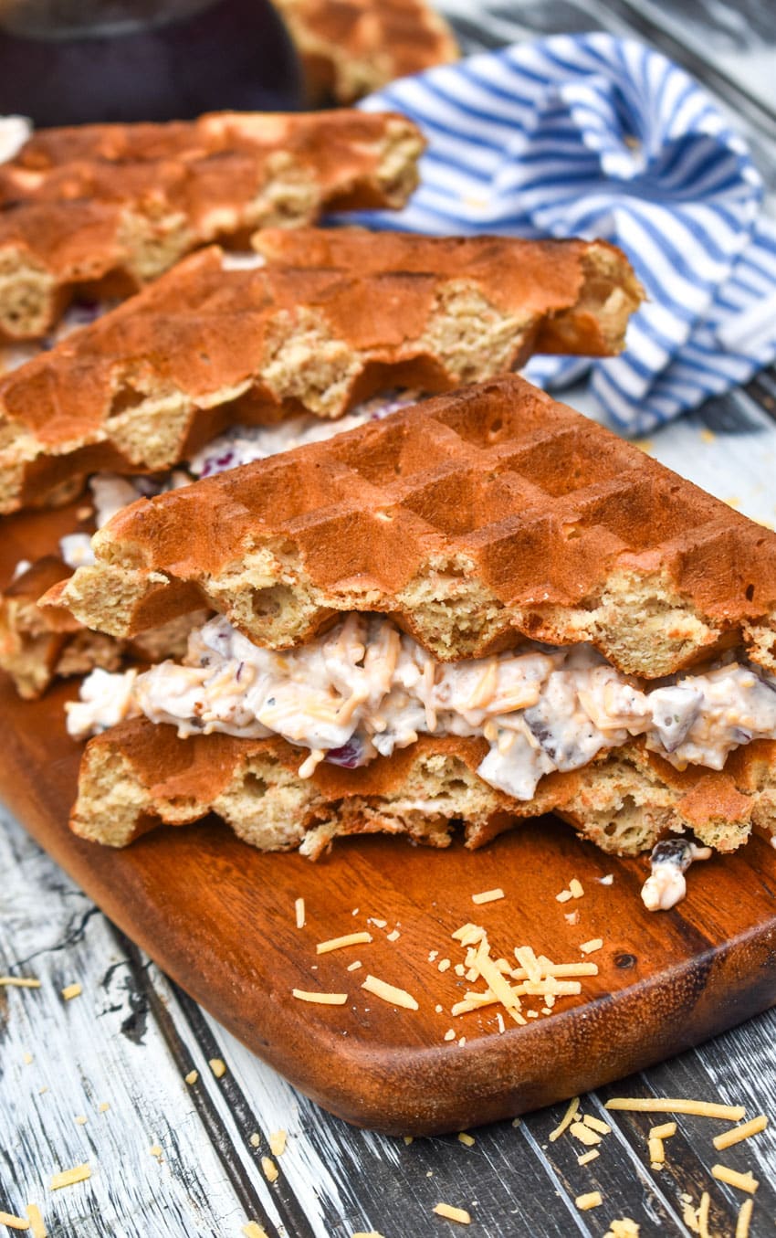 maple bacon chicken salad in between sliced waffles on a wooden cutting board