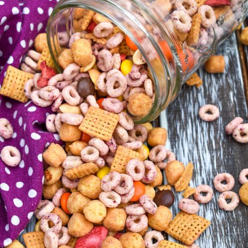 peanut butter and jelly trail mix spilling out of a glass jar onto a wooden table