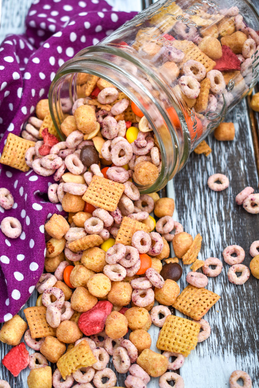 Peanut Butter And Jelly Trail Mix peanut butter and jelly trail mix spilling out of a glass jar onto a wooden table