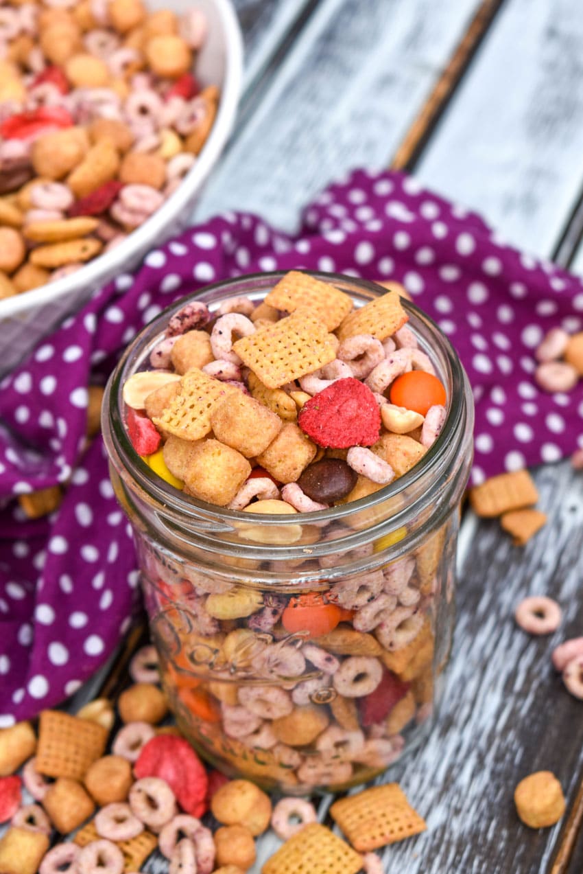 peanut butter and jelly trail mix in a small glass jar on a wooden table