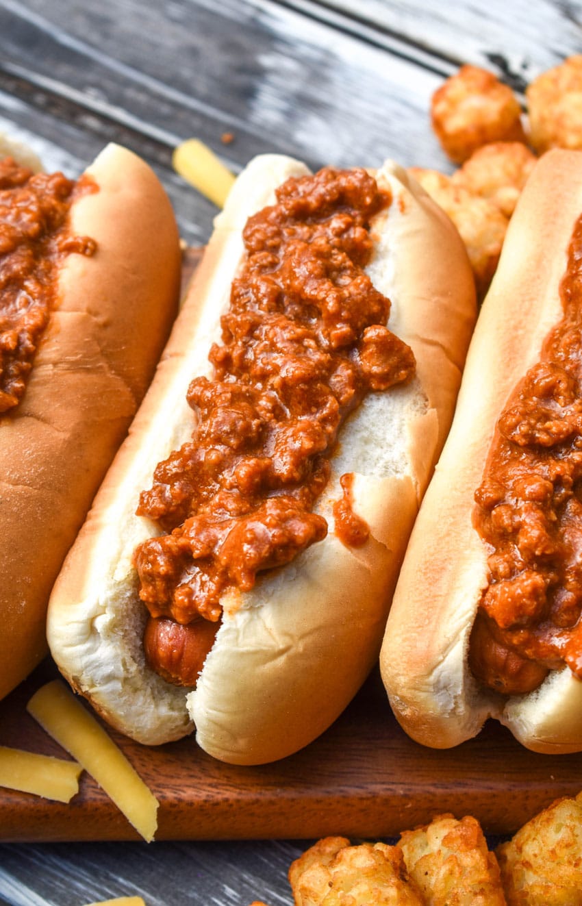 quick and easy hot dog chili on top of hot dogs in buns arranged in a row on a wooden cutting board