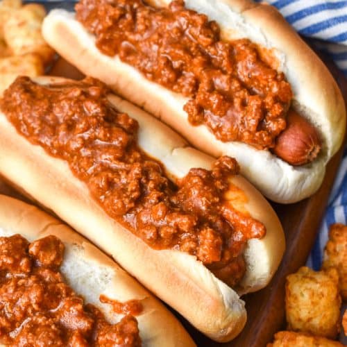 quick and easy hot dog chili on top of hot dogs in buns arranged in a row on a wooden cutting board
