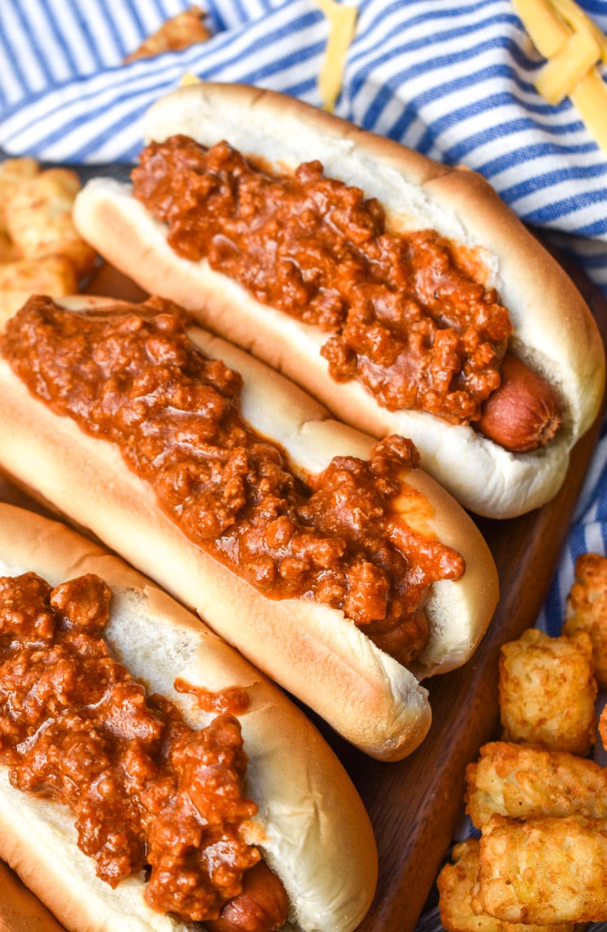 quick and easy hot dog chili on top of hot dogs in buns arranged in a row on a wooden cutting board