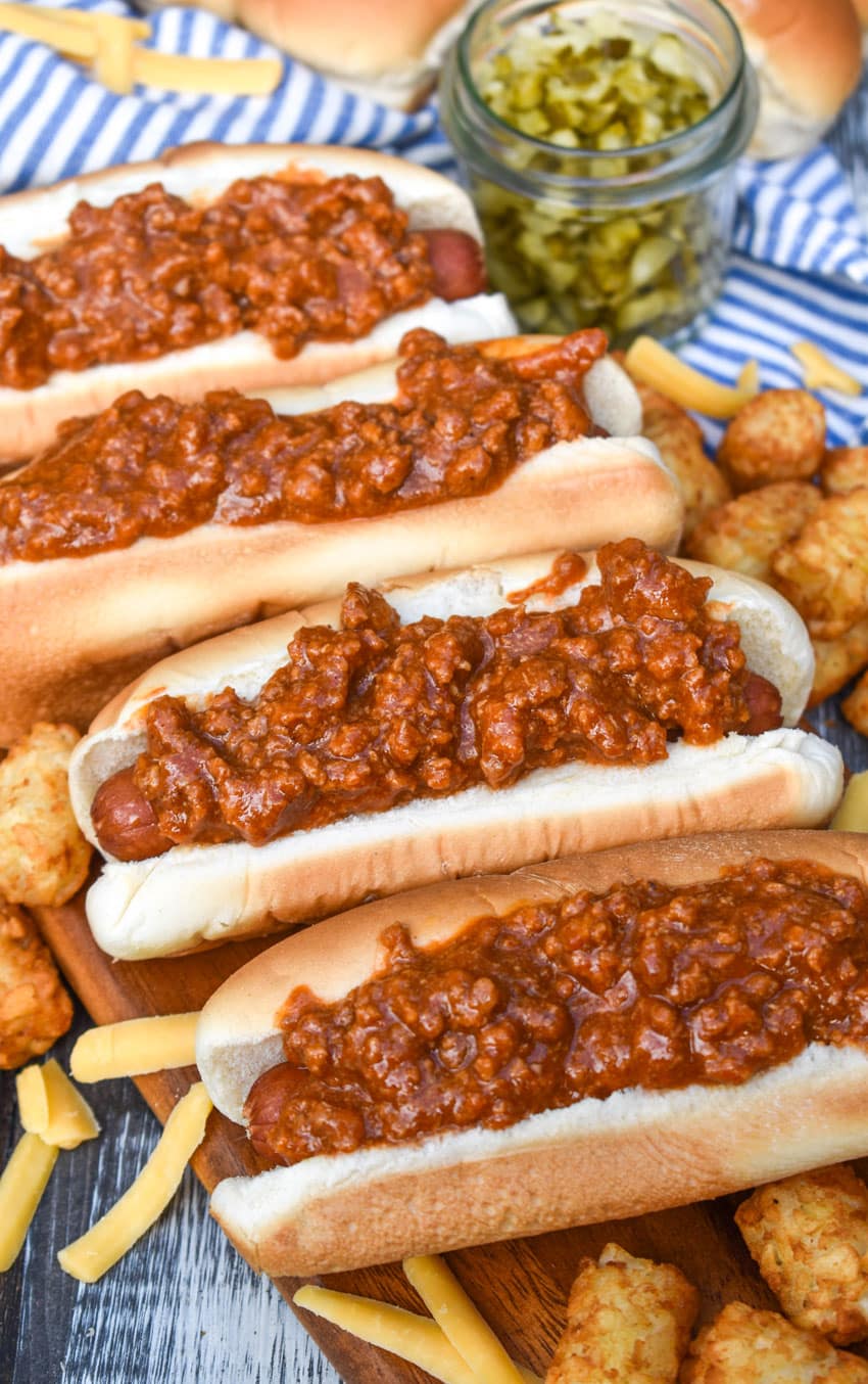 quick and easy hot dog chili on top of hot dogs in buns arranged in a row on a wooden cutting board