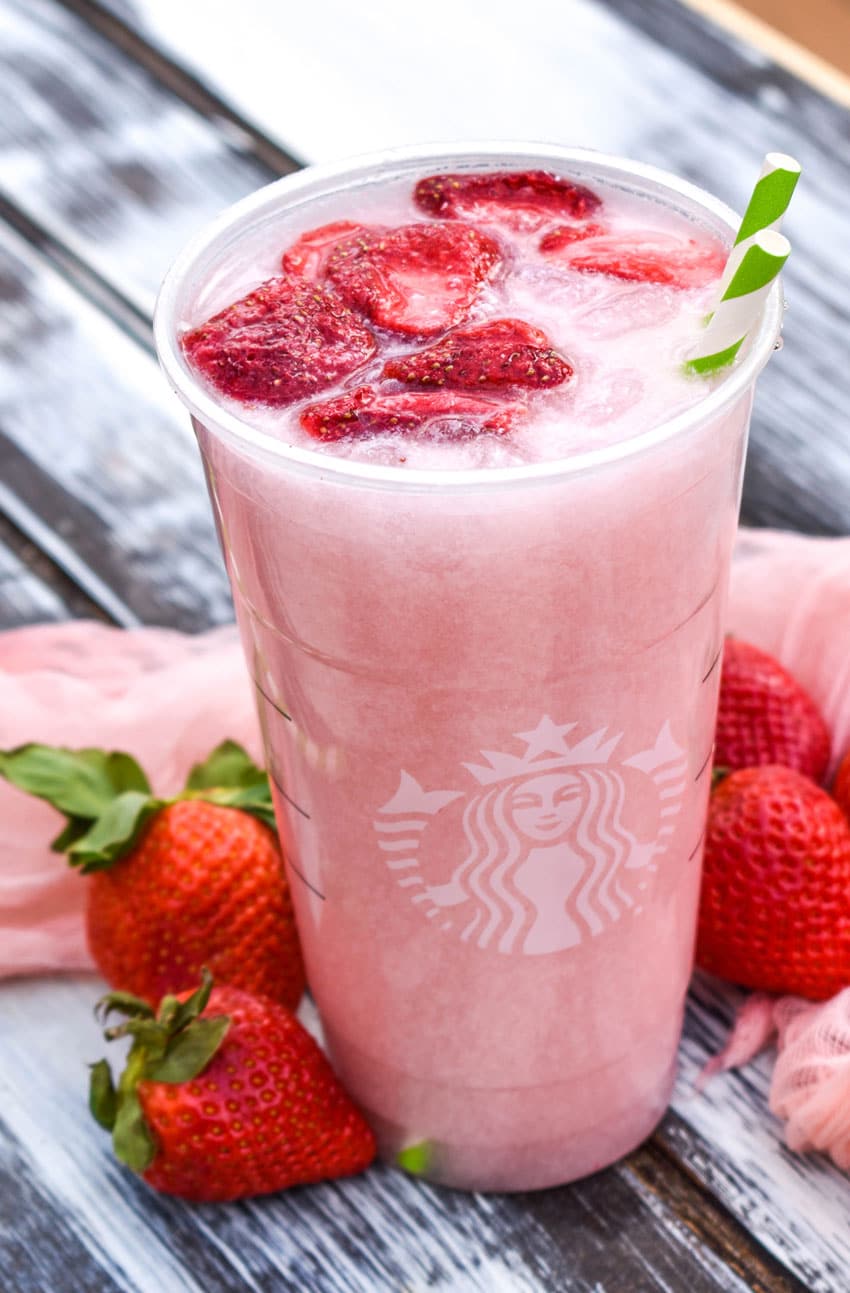 copycat starbucks pink drink in a plastic cup with dehydrated strawberries floating on top with two paper straws