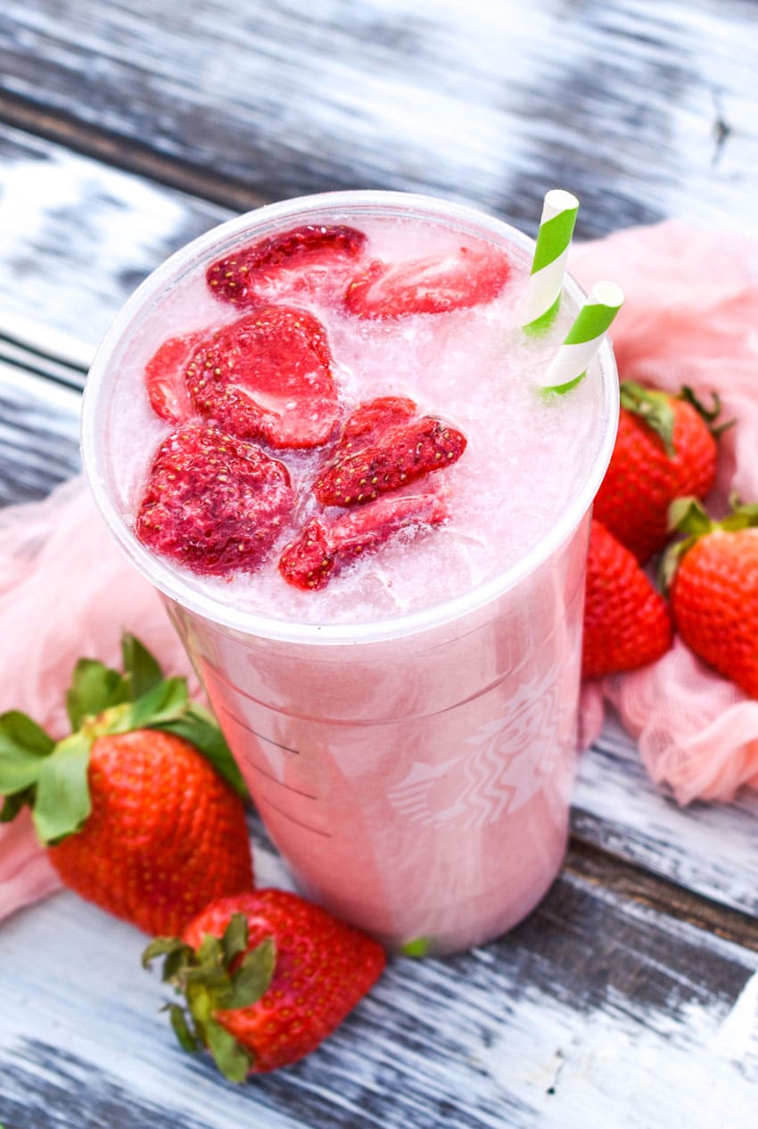 copycat starbucks pink drink in a plastic cup with dehydrated strawberries floating on top with two paper straws