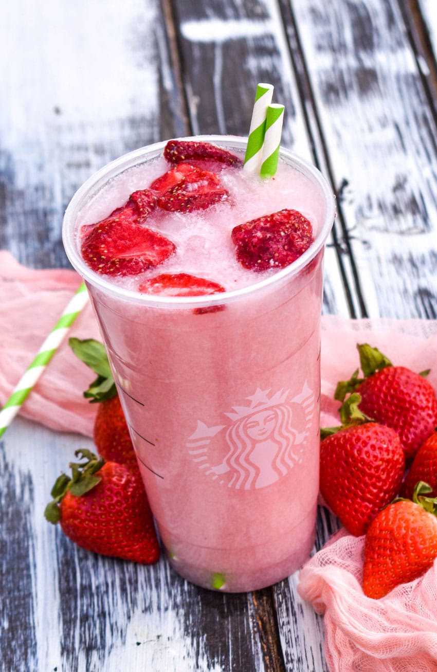 copycat starbucks pink drink in a plastic cup with dehydrated strawberries floating on top with two paper straws