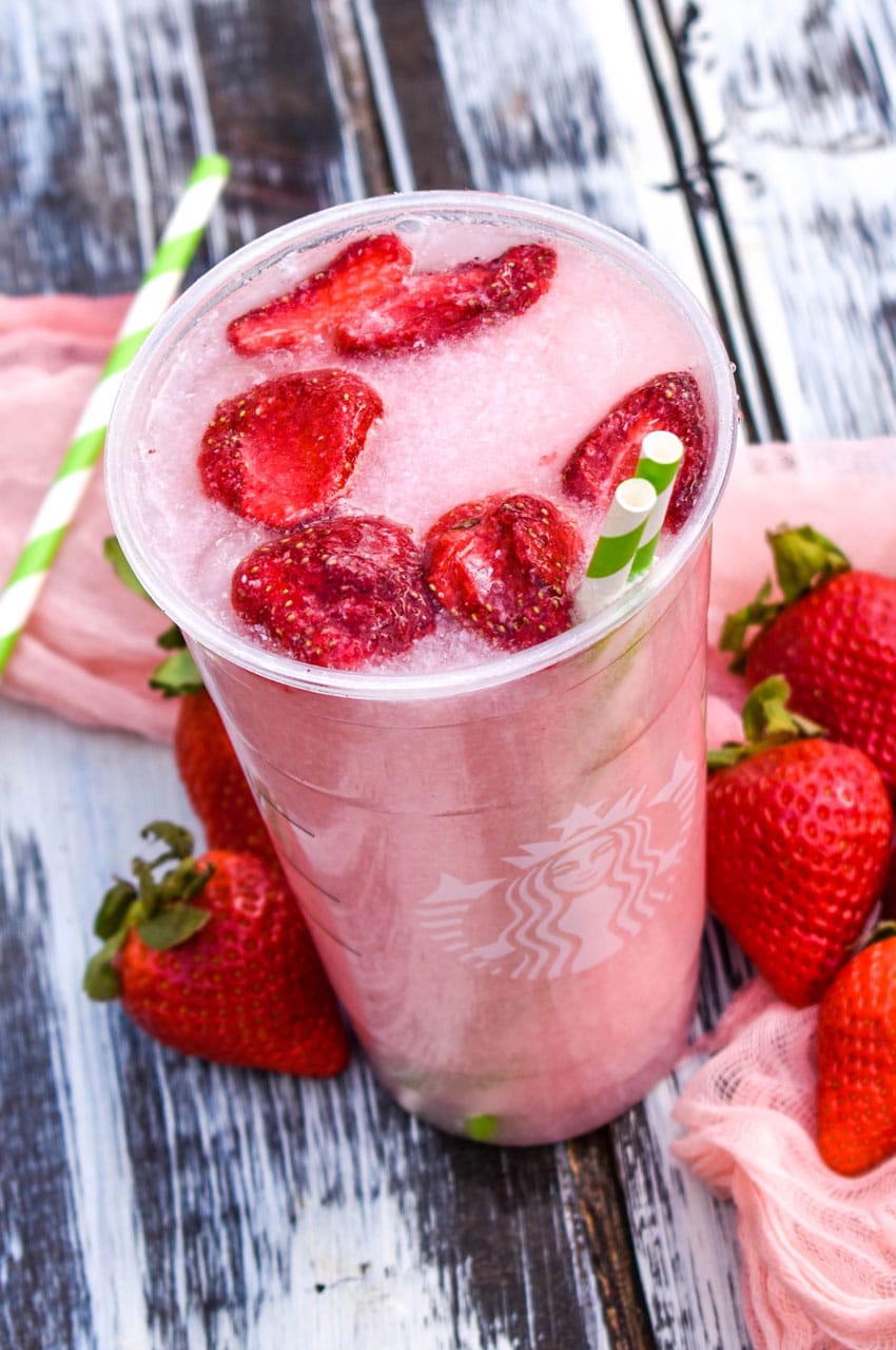 copycat starbucks pink drink in a plastic cup with dehydrated strawberries floating on top with two paper straws