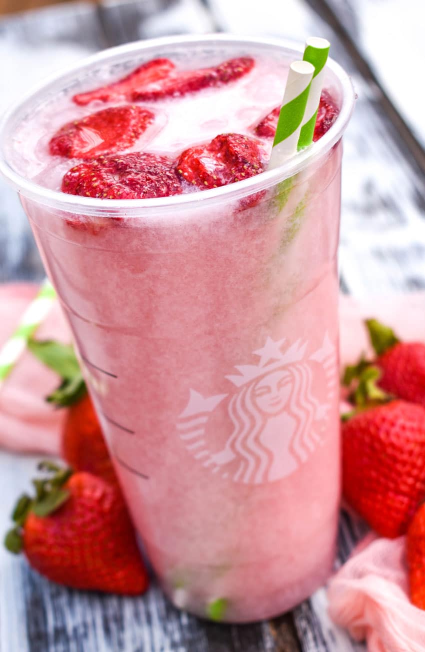 copycat starbucks pink drink in a plastic cup with dehydrated strawberries floating on top with two paper straws
