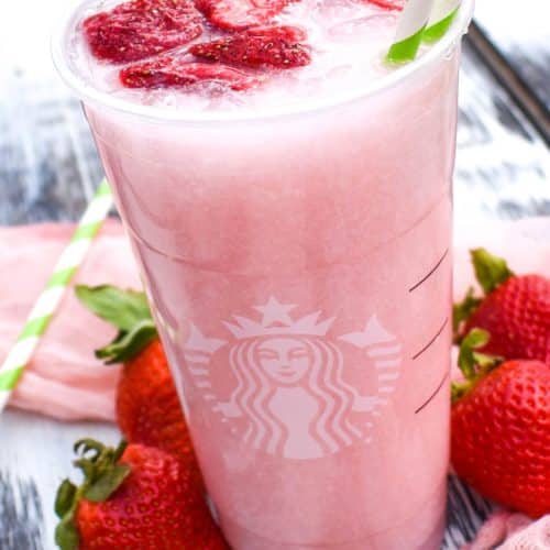 copycat starbucks pink drink in a plastic cup with dehydrated strawberries floating on top with two paper straws