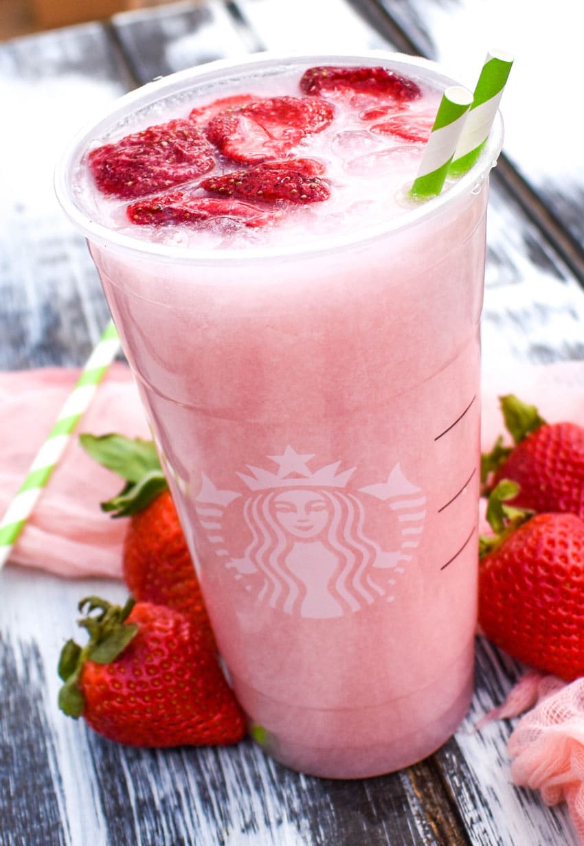 copycat starbucks pink drink in a plastic cup with dehydrated strawberries floating on top with two paper straws
