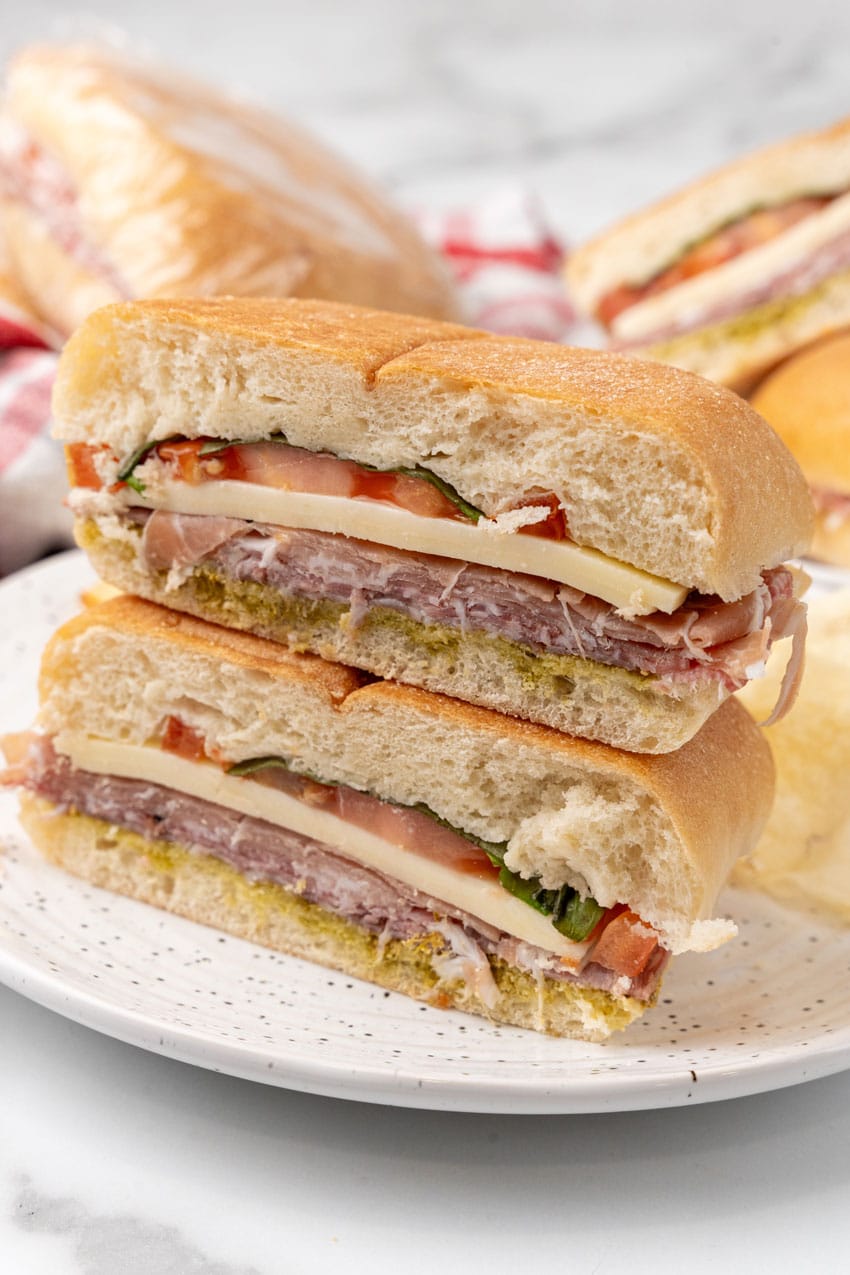 two halves of an italian pressed picnic sandwich stacked together on a white plate