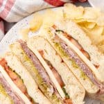 slices of an italian pressed picnic sandwich on a white plate with potato chips on the side