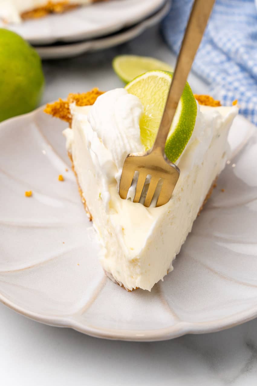 a gold fork digging into a slice of no bake key lime cheesecake on a white dessert plate