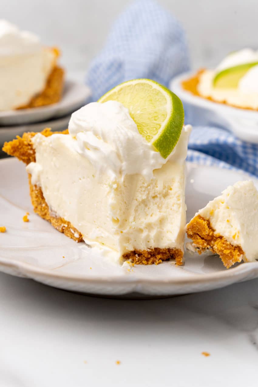 a slice of no bake key lime pie cheesecake with a bite taken out on a white dessert plate