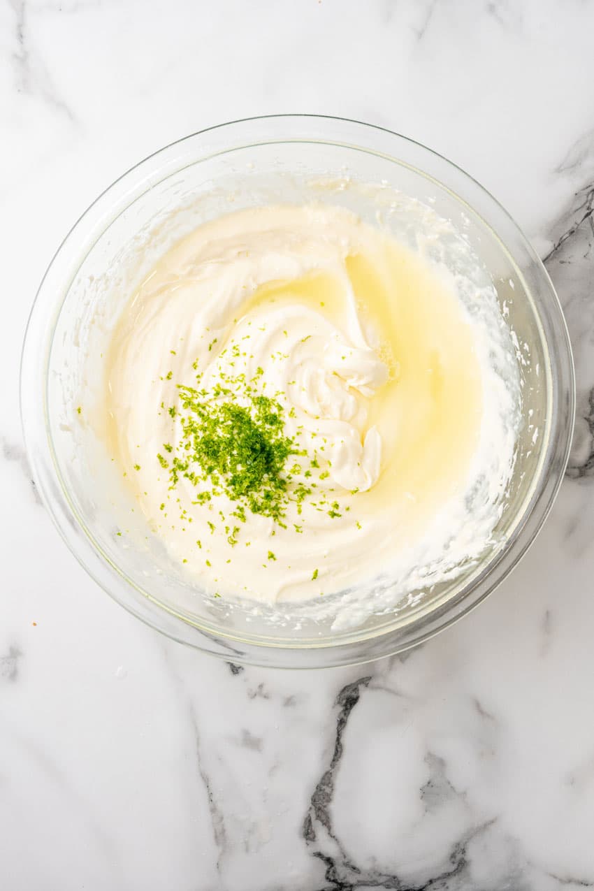 lime zest and lime juice resting on creamy cheesecake filling in a glass mixing bowl