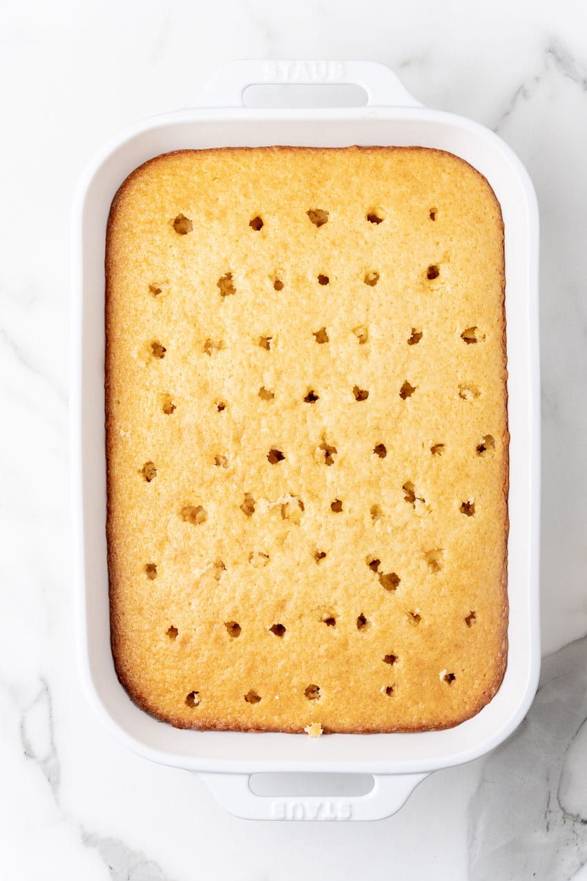 a yellow cake in a white baking dish with holes poked in the surface