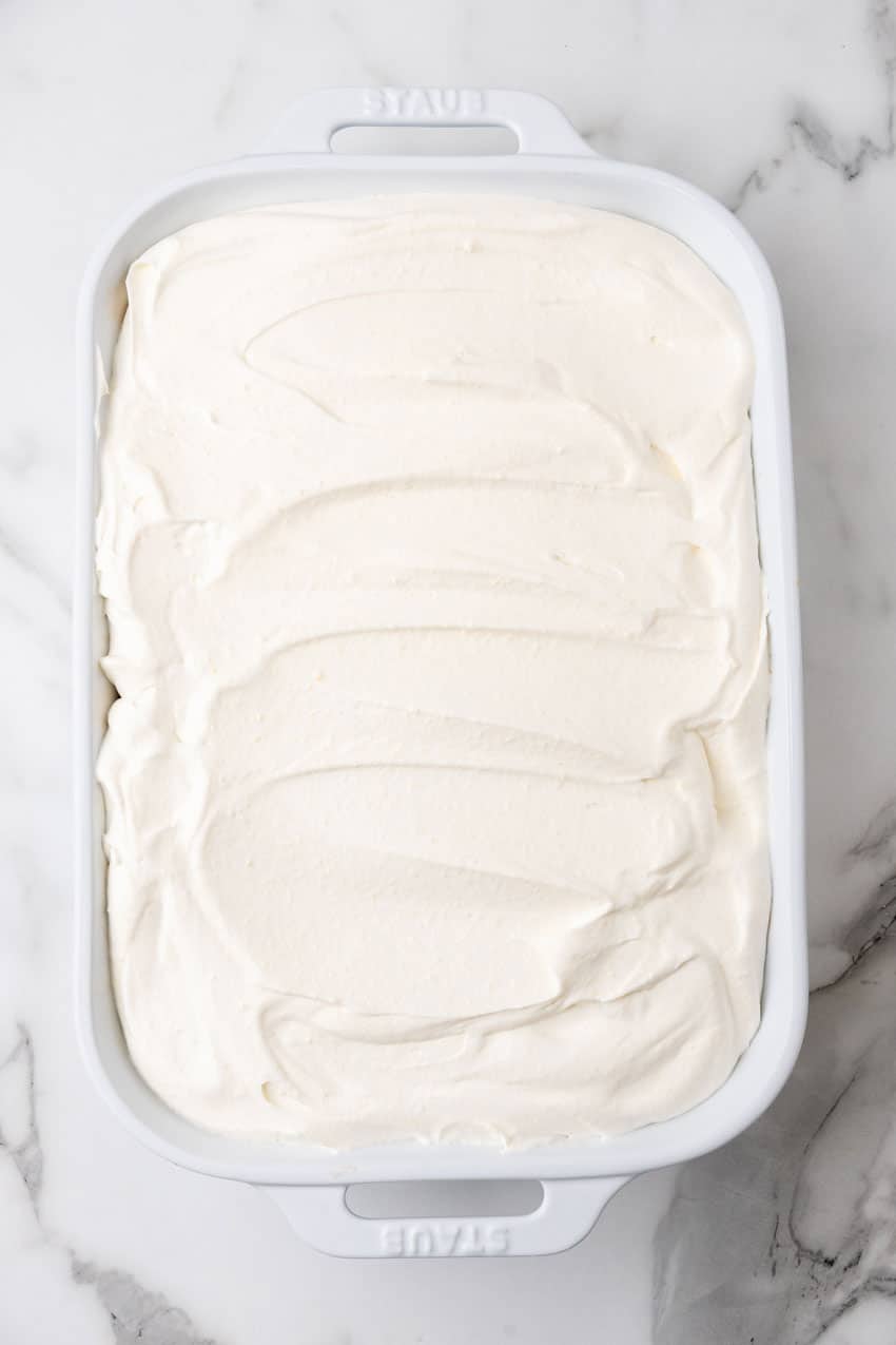whipped cream mixture spread over an orange creamsicle poke cake in a white baking dish
