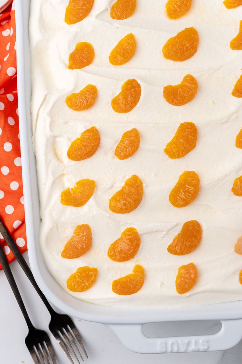 a close up of an orange creamsicle poke cake in a white casserole dish