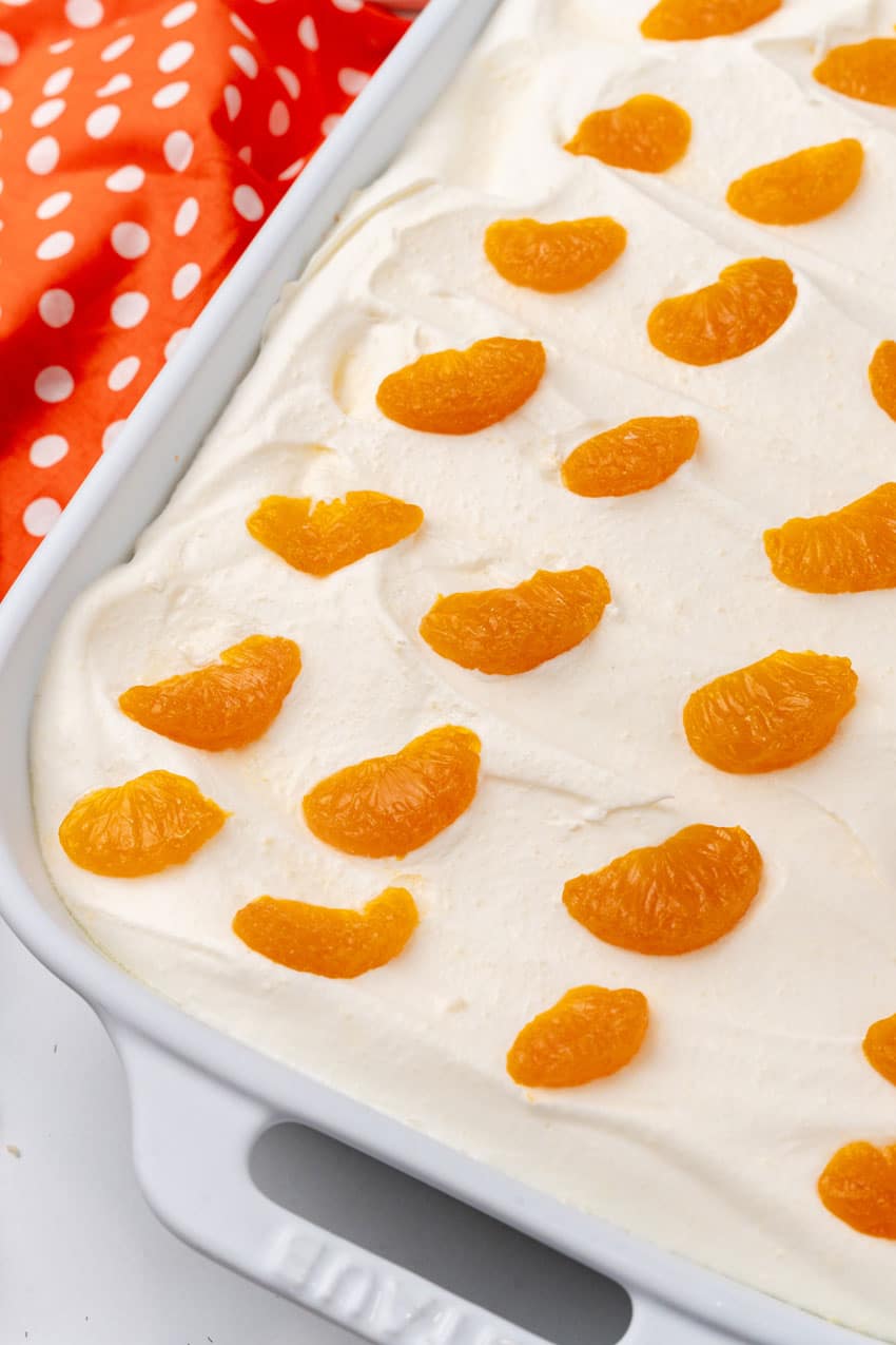 a close up of an orange creamsicle poke cake in a white casserole dish