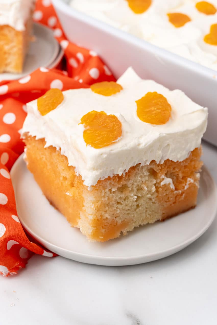 a slice of orange creamsicle poke cake on a small white dessert plate