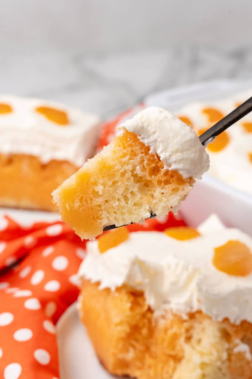 a black fork holding up a scoop of orange creamsicle poke cake