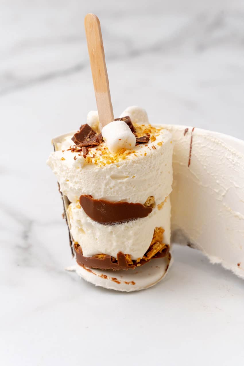 a paper cup being pulled away from a frozen s'mores ice cream popsicle