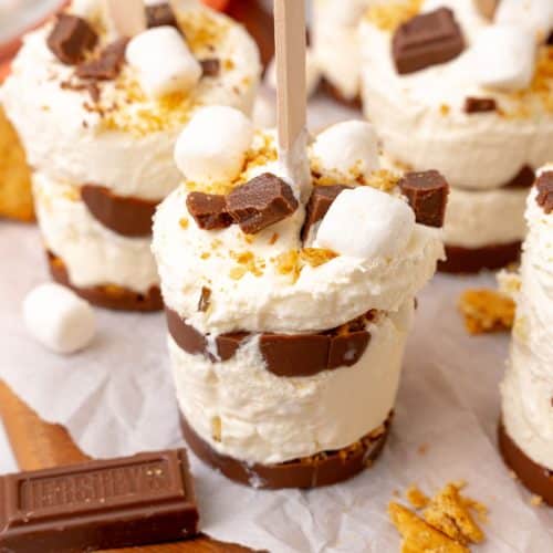 frozen s'mores ice cream pops on a white piece of parchment paper on a wooden cutting board