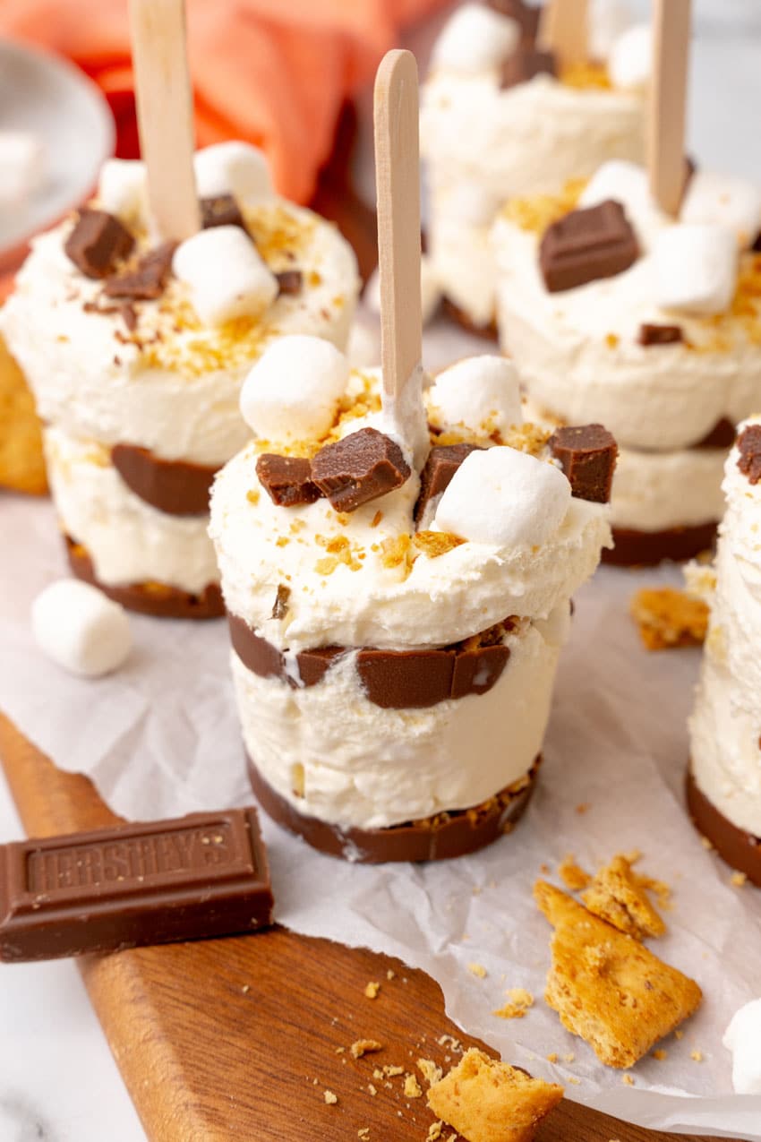 frozen s'mores ice cream pops on a white piece of parchment paper on a wooden cutting board