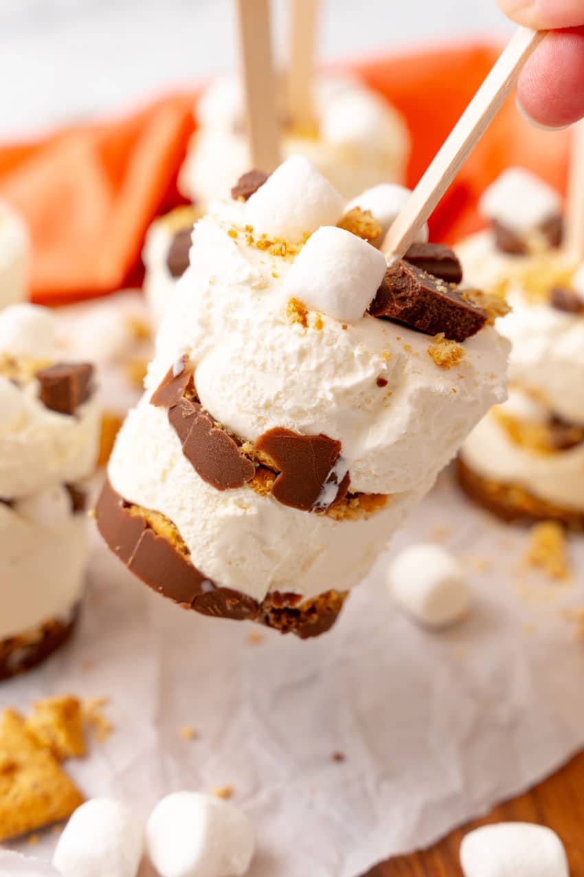 a hand holding up a smores ice cream pop over a sheet of white parchment paper