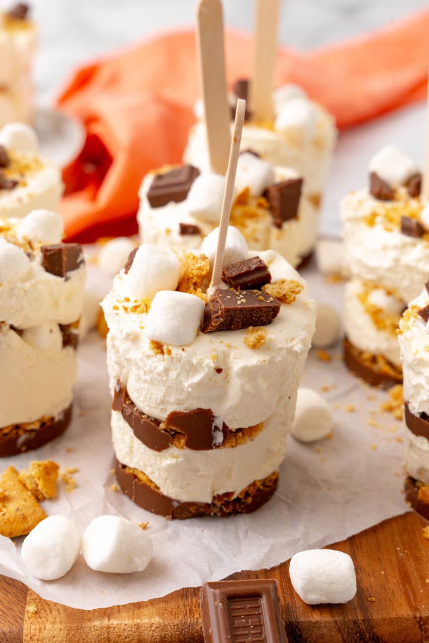 S'mores Ice Cream Pops s'mores pops on a white piece of parchment paper on a wooden cutting board
