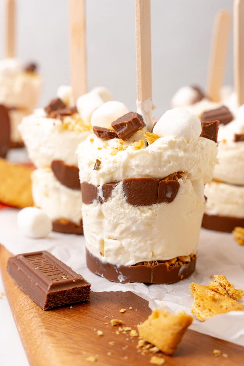 frozen s'mores ice cream pops on a white piece of parchment paper on a wooden cutting board