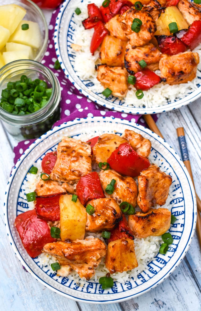 air fryer pineapple chicken over steamed white rice topped with sliced green onions in two white bowls