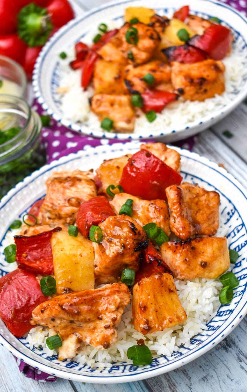 air fryer pineapple chicken over steamed white rice topped with sliced green onions in two white bowls