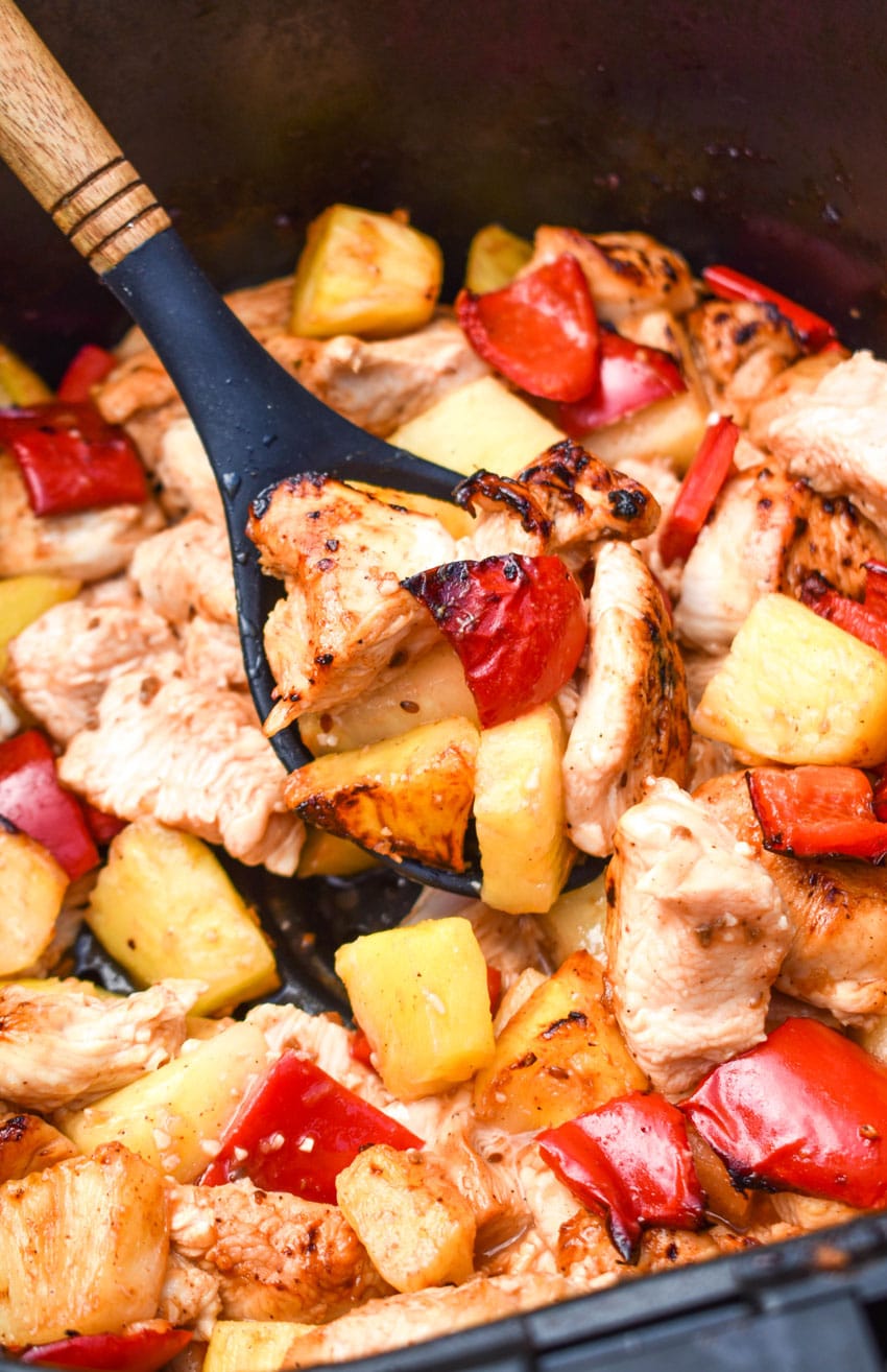 a wooden handled spoon scooping pineapple chicken out of the basket of an air fryer
