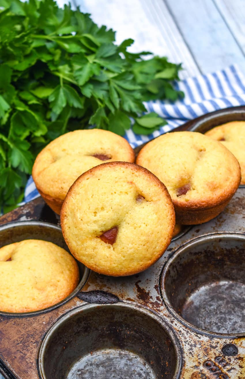 corn dog muffins stacked together on the edge of a metal muffin tin