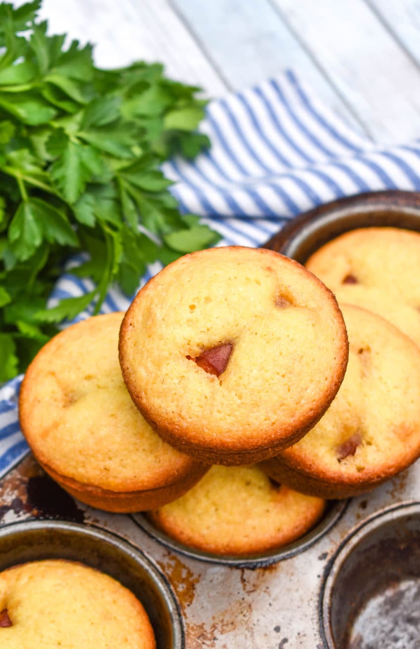 corn dog muffins stacked together on the edge of a metal muffin tin
