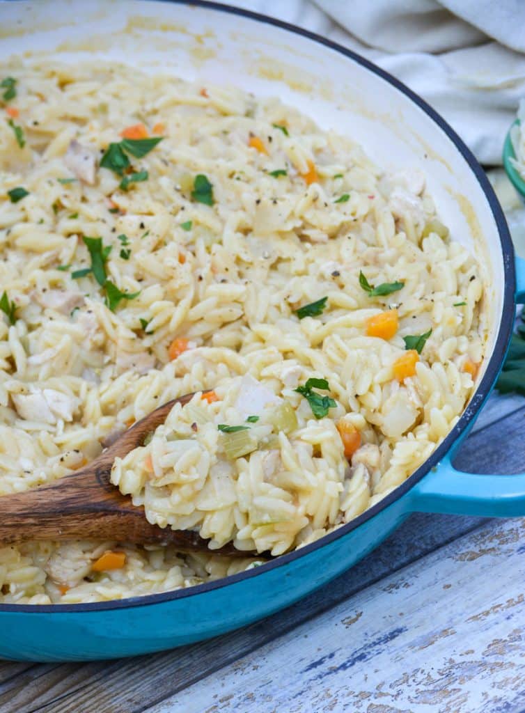 a wooden spoon scooping creamy chicken and orzo pasta out of a cast iron skillet