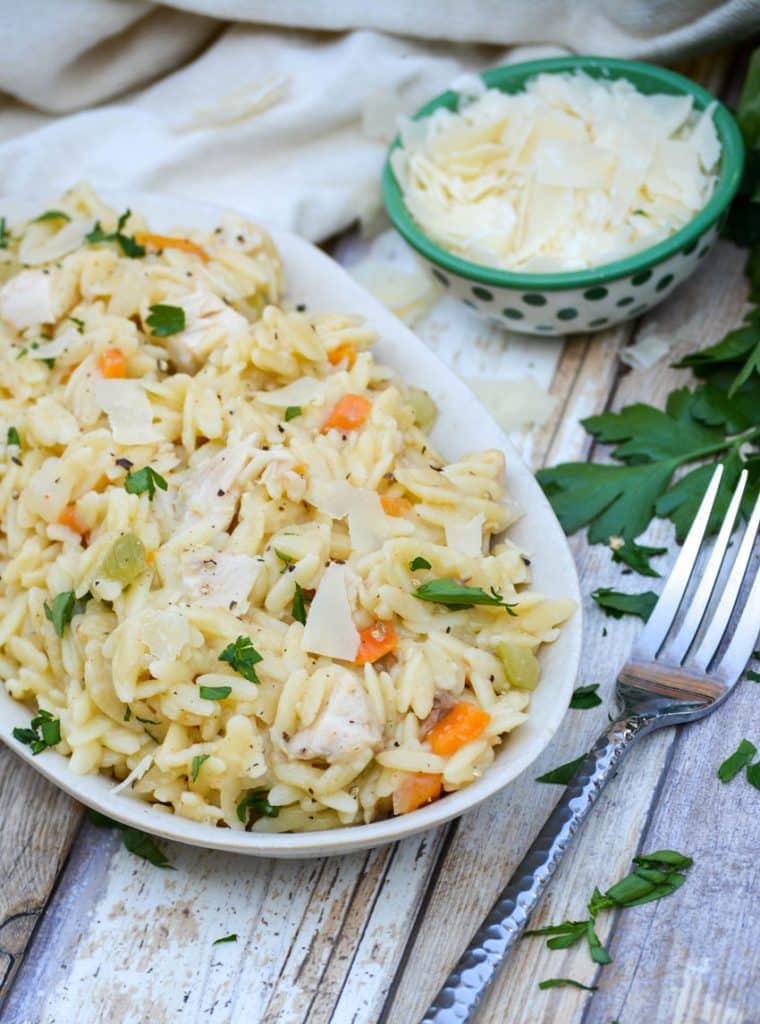 creamy chicken and orzo pasta in a small white dish with silver fork and fresh herbs on the side