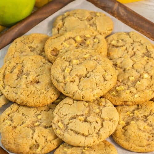 caramel apple cookies stacked on a parchment paper lined baking sheet